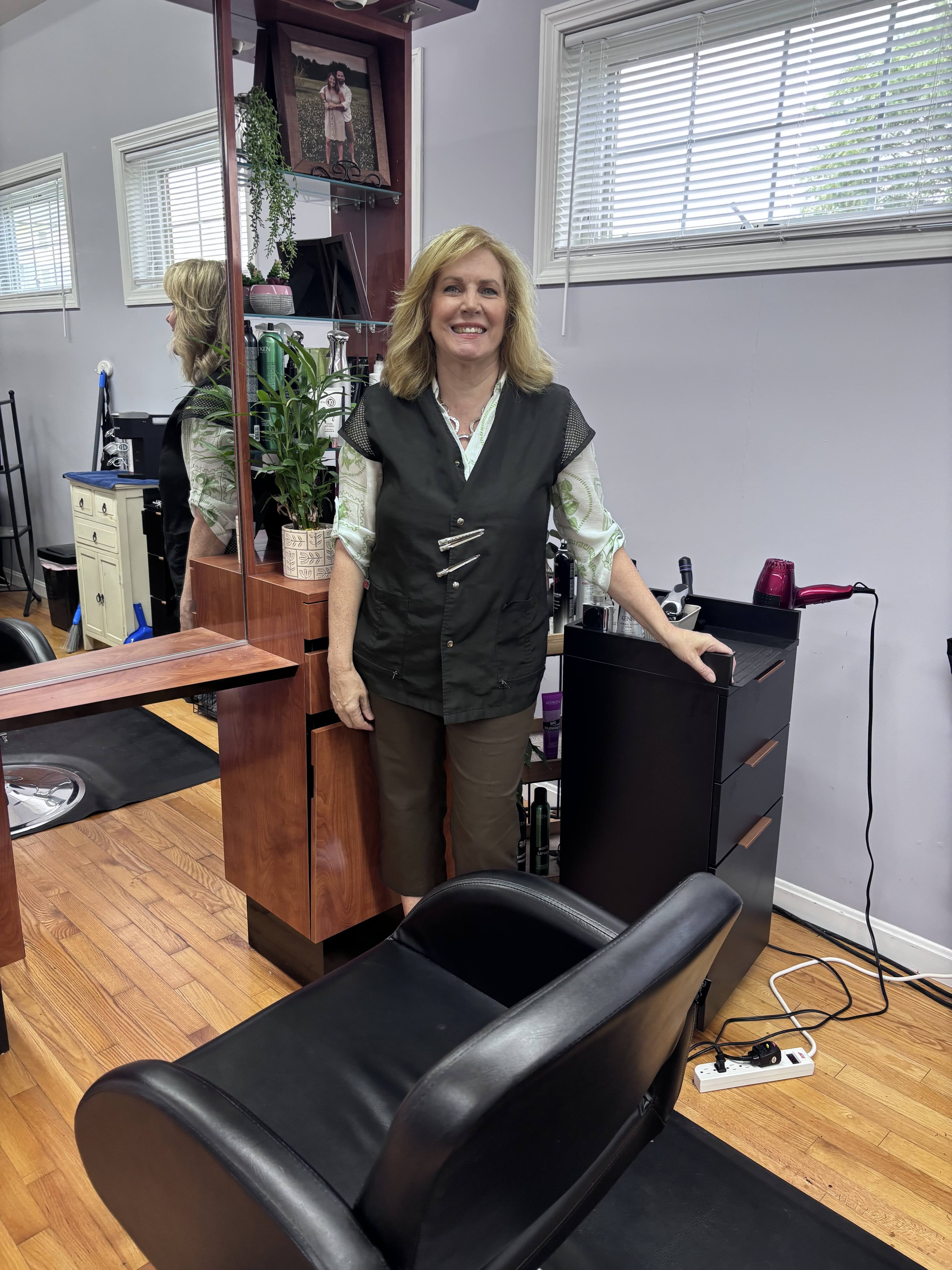 Karen smiling beside her styling chair and station in the salon